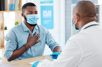 Patient talking to doctor about covid symptoms. African american man talking to a gp about chest pain in the clinic. Doctor in a consult with a patient about corona. Patient and doctor wearing masks.