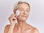 A mature caucasian woman using a cotton pad to remove makeup during a selfcare grooming routine. Older model  applying cleanser to her face against pink copyspace background