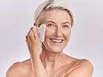 Studio Portrait of a mature woman woman using a gua sha stone for deep cell penetration against wrinkles. Happy older woman using anti ageing tool against purple copyspace background