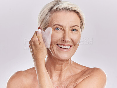 Buy stock photo Skin care, hygiene and grooming by mature woman using a gua sha stone while giving herself a face massage. Happy senior female dace enjoying a beauty skincare routine to refresh and smooth wrinkles