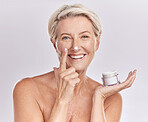 Portrait of one happy mature caucasian woman posing topless against a purple copyspace background. Ageing woman applying cream, moisturiser, sunblock during a skincare routine in a studio