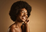 Happy African American woman with a natural afro posing against brown studio copyspace background. Young beautiful black female model looking trendy, powerful and sensual with smooth glowing skin