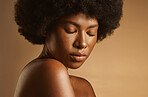 Confident African American woman with a natural afro posing against brown studio copyspace background. Young beautiful black female model looking trendy, powerful and sensual with smooth glowing skin