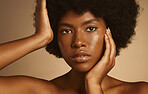 Young African woman with afro hair and glowing radiant skin posing against a brown studio background. One female only wearing natural makeup and looking confident with flawless complexion