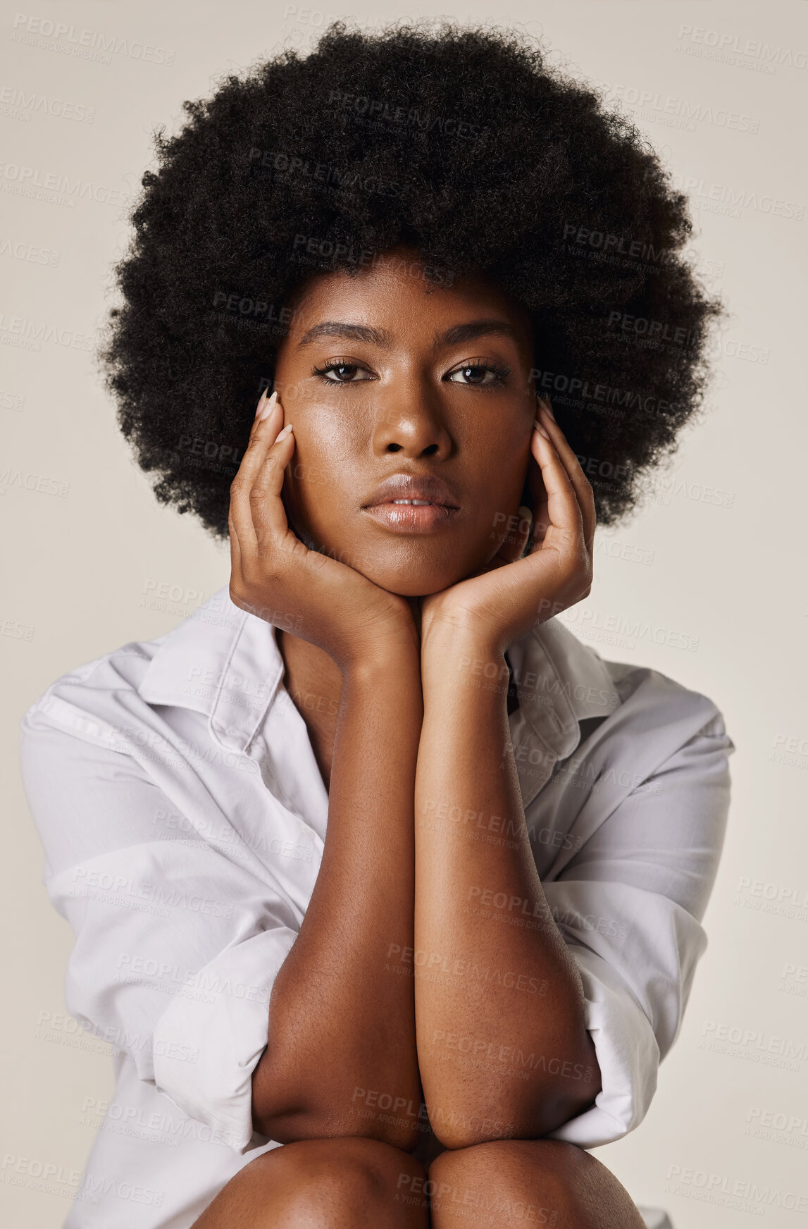 Buy stock photo Gorgeous african american woman with beautiful afro wearing a white shirt and sitting with her hands around her face. Young female with glowing skin sitting against a plain background 