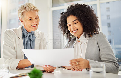 Two diverse smiling businesswomen working together on corporate plans in an office boardroom. Mature caucasian and young mixed race businesswoman reading paperwork and analysing reports