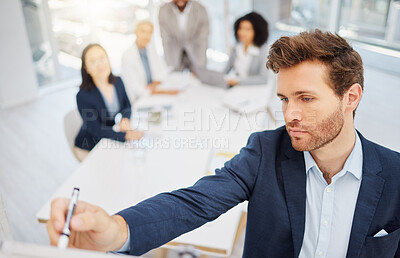 One focused young caucasian businessman from above using a whiteboard to write notes while leading a presentation with his colleagues during a meeting in an office boardroom