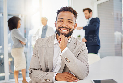 Portrait of a confident young mixed race businessman smiling with hand on chin in an office with his colleagues in the background. Ambitious entrepreneur and determined leader ready for success in his startup with his team