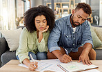 Young mixed race couple working on their budget at a table together at home. Hispanic husband and wife sitting on the couch while planning and paying bills