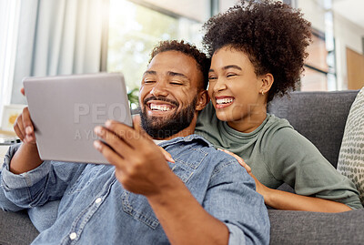 Buy stock photo Mixed race couple smiling while using a digital tablet together at home. Joyful hispanic boyfriend and girlfriend laughing while relaxing and using social media on a digital tablet in the lounge at home