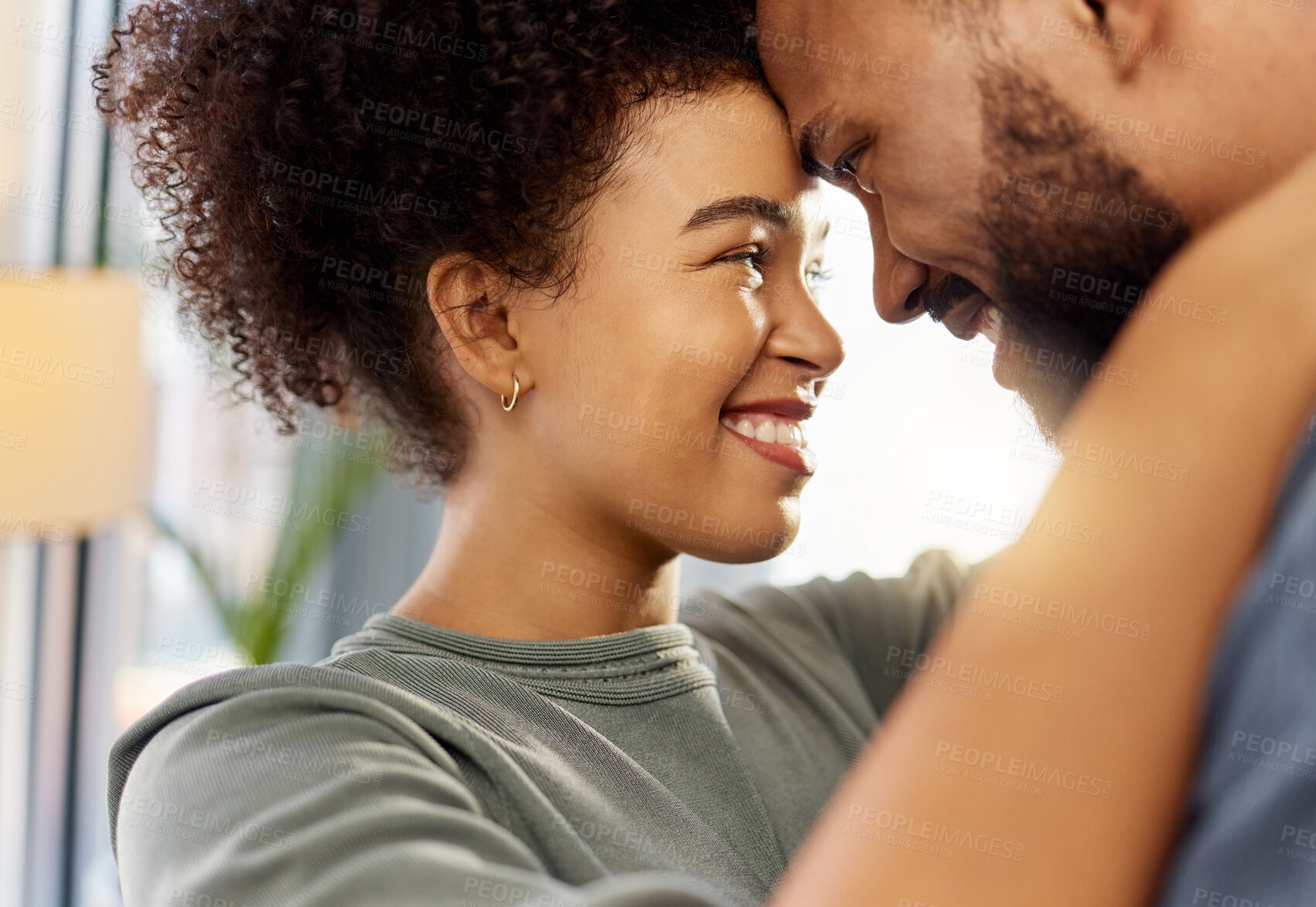 Buy stock photo Happy mixed race couple hugging while relaxing at home. Carefree hispanic husband and wife smiling while staring into each other’s eyes lovingly and hugging in the lounge at home