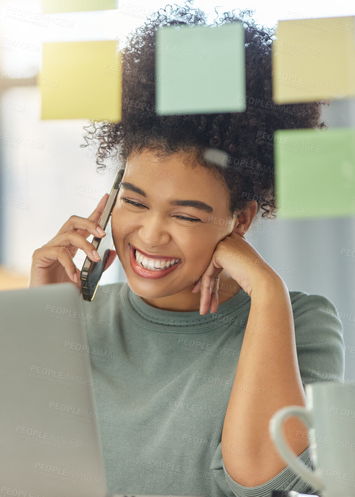 Buy stock photo Young happy mixed race woman on a call with her phone while working a laptop sitting at a table at home. Joyful hispanic female with a curly afro laughing while talking on the phone alone in the lounge at home