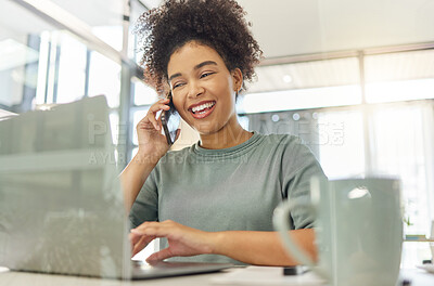 Buy stock photo Happy mixed race woman on a call with her phone while working on a laptop sitting at a table at home. Cheerful hispanic female with a curly afro laughing while talking on the phone and typing an email alone in the lounge at home