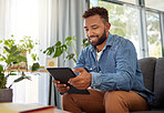 Handsome bachelor reading on his digital tablet. Happy bachelor enjoying his day at home relaxing. Always connected to the online world with his wireless tablet. Young man resting on his couch