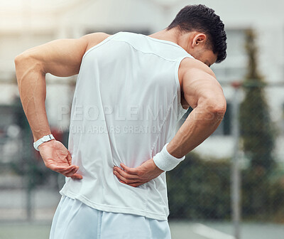 Rearview unknown mixed race tennis player suffering from backache in court game. Hispanic fit athlete in pain while holding and rubbing back injury in match. Sporty man standing alone in sports club