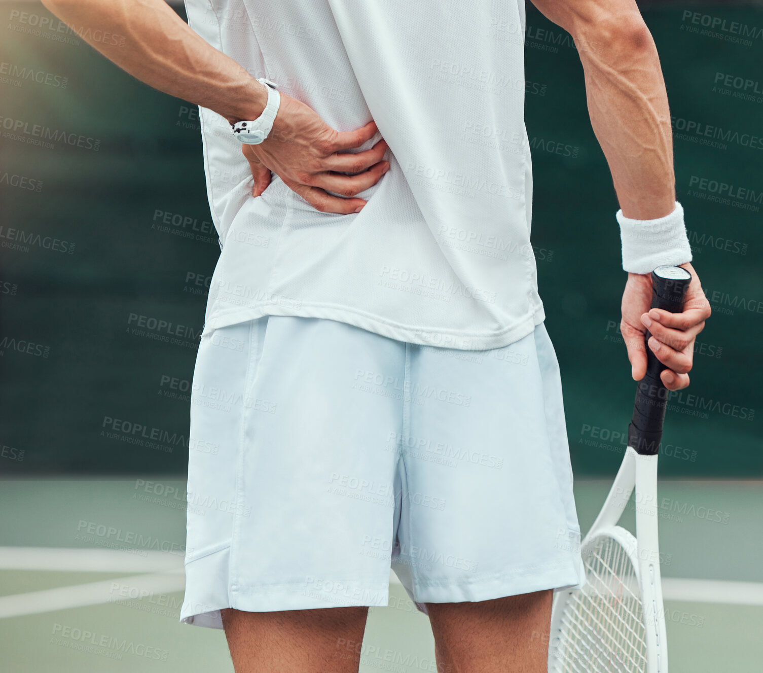 Buy stock photo Rearview unknown mixed race tennis player suffering from backache in court game. Hispanic fit athlete in pain while holding and rubbing back injury in match. Sporty man standing alone in sports club