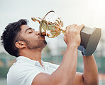One indian tennis player drinking from a trophy while celebrating success after winning a court game. Ethnic fit athlete holding prize award after a match. Active healthy man playing competitive sport
