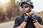 Athletic sportsman wearing glasses and gloves while tying his cycling helmet. Male cyclist putting on a helmet for safety. Professional cyclist getting ready for a ride on a mountain road