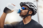 Close up of male cyclist taking a break and drinking water from a bottle. Fit young man wearing glasses and a helmet while drinking water and standing outside. Athletic man cycling in nature environment