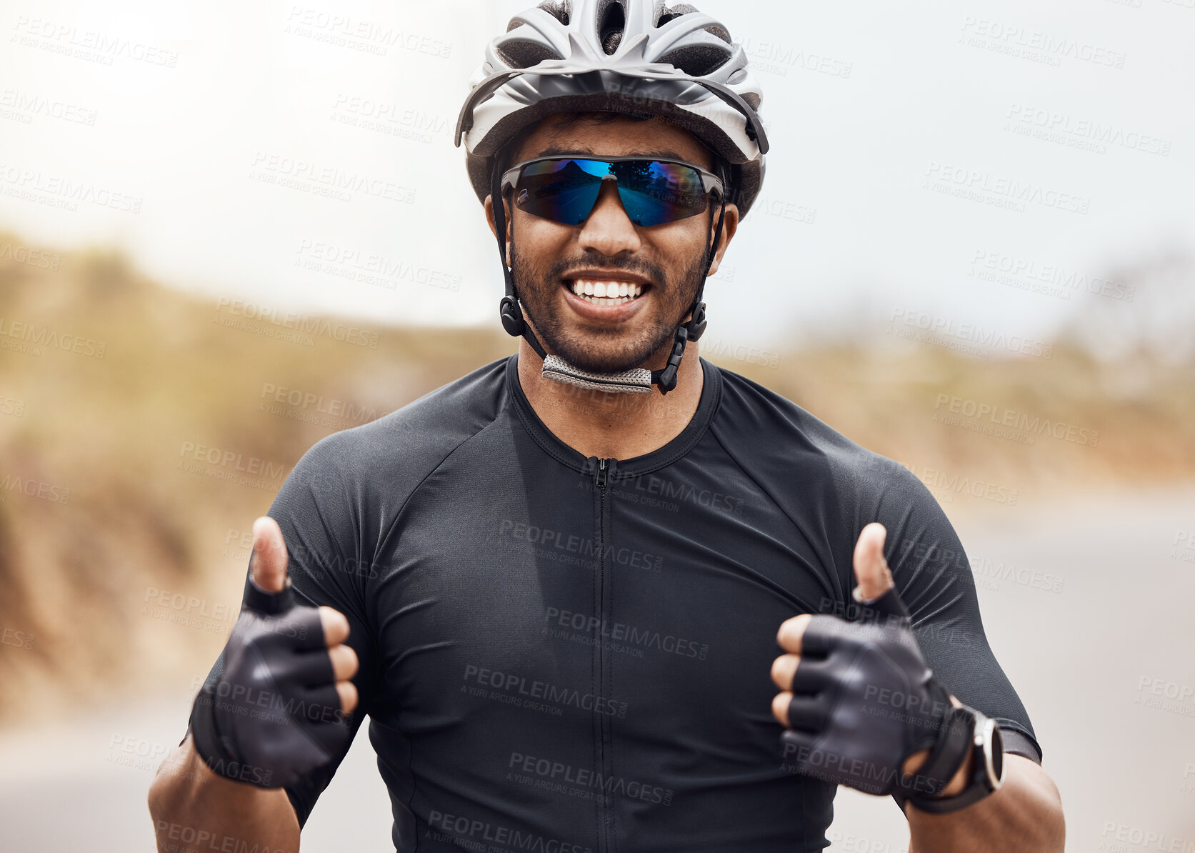 Buy stock photo One young man showing thumbs up while cycling outside. Happy male wearing helmet and glasses winning first in competition race. Pleased with his time results and enjoying a break from cardio training