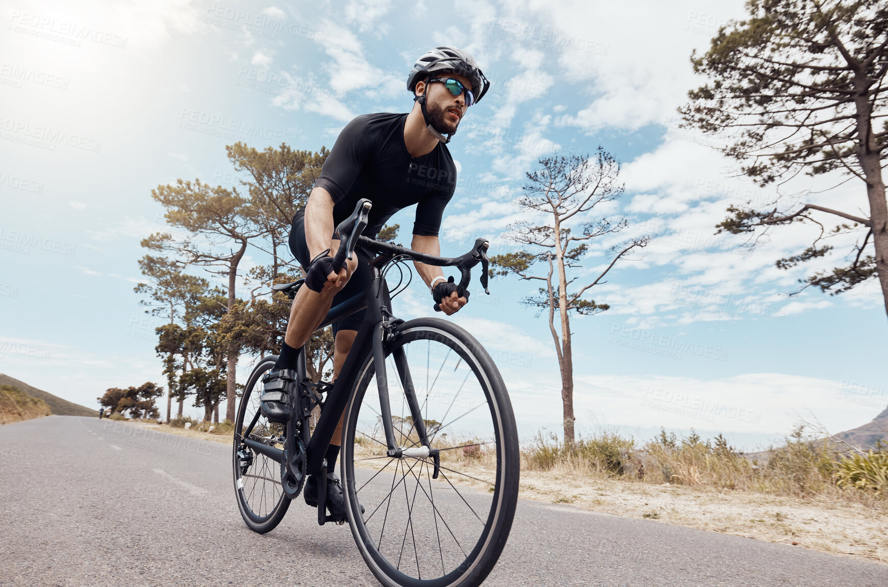 Buy stock photo One athletic young man cycling outside. Sporty fit male wearing helmet and glasses while riding a bike on a scenic mountain road with the sky in the background for exercise