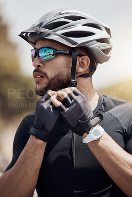 Buy stock photo Closeup of male cyclist wearing glasses and gloves while tying or removing his cycling helmet. Athletic young man putting on a helmet for safety. Professional cyclist getting ready for a ride or training outdoors