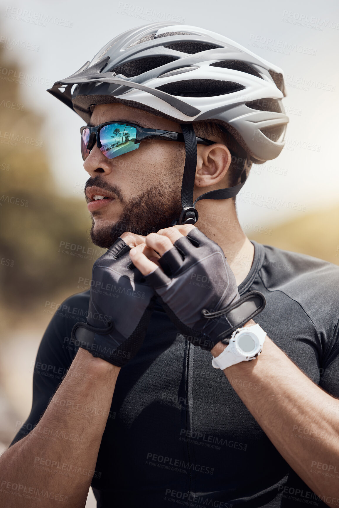 Buy stock photo Closeup of male cyclist wearing glasses and gloves while tying or removing his cycling helmet. Athletic young man putting on a helmet for safety. Professional cyclist getting ready for a ride or training outdoors