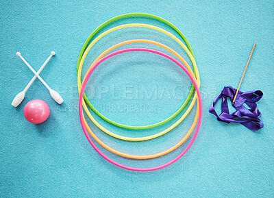 Rhythmic gymnastics equipment on blue background or carpet. Neon coloured hula hoops, dance ribbon, pink ball and gymnastic clubs from above