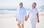 Happy mixed race senior couple holding hands while walking on the beach together. Mature couple traveling and enjoying retirement