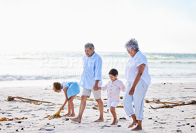 Buy stock photo Grandparents and grandchildren holding hands while walking along the beach. Senior couple enjoying summer vacation with grandson and granddaughter by the sea