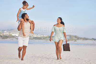 Happy mixed race family walking along the beach for a family picnic. Adorable little sitting on her fathers shoulders while enjoying time by the beach with her two parents