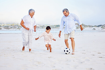 Buy stock photo Active grandparents playing soccer on the beach with their grandson. Little boy kicking ball with his grandmother and grandfather on shore