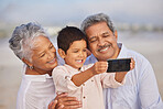 Grandparents with grandson at the beach holding mobile and taking selfie or doing video call with family during vacation by the sea. Adorable little boy taking a picture with his grandmother and grandfather