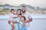 Portrait of a happy mixed race family standing together on the beach. Loving parents spending time with their two children during family vacation by the beach