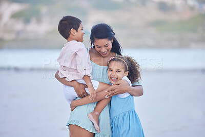 Loving mixed race mother hugging her children while enjoying family time at the beach. Little girl and boy enjoying summer vacation by the sea with their mom
