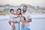 Portrait of a cheerful mixed race family laughing while standing together on the beach. Loving parents spending time with their two children during family vacation by the beach