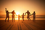 Rear view of a three generation family silhouetted on the beach while jumping together. Cheerful family with two children, two parents and grandparents holding hands and watching the sunset at the beach