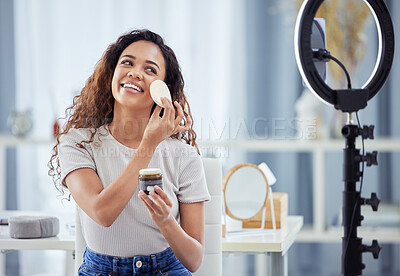 One hispanic woman recording a makeup tutorial for her beauty blog with her phone while sitting at home. African american female influencer live streaming her cosmetic review and recommendation online