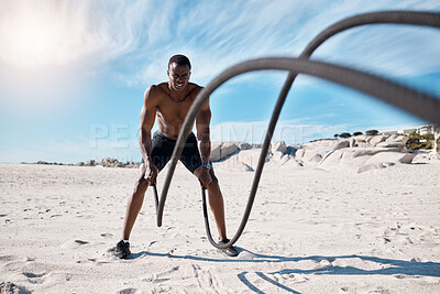 Buy stock photo Full length fit and active african american man using battle ropes to workout on a beach alone in the day. Strong and muscular black man training shirtless in nature. Focused on health and strength