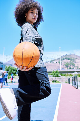 Portrait of one trendy mixed race woman with an afro holding a basketball and posing on a court outside. Fashionable hispanic with curly hair feeling confident. African American showing street style