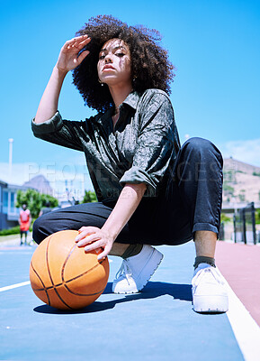Cool young hispanic woman with curly hair lifting her afro from her face holding a basketball on the court. Serious African American basketball player on squatting on the court before a match