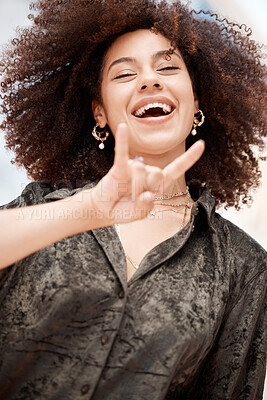 Young mixed race woman with curly afro hair smiling and laughing while expressing a rock and roll symbol hand gesture outside. Carefree, cool and confident female making horn sign to show good vibes