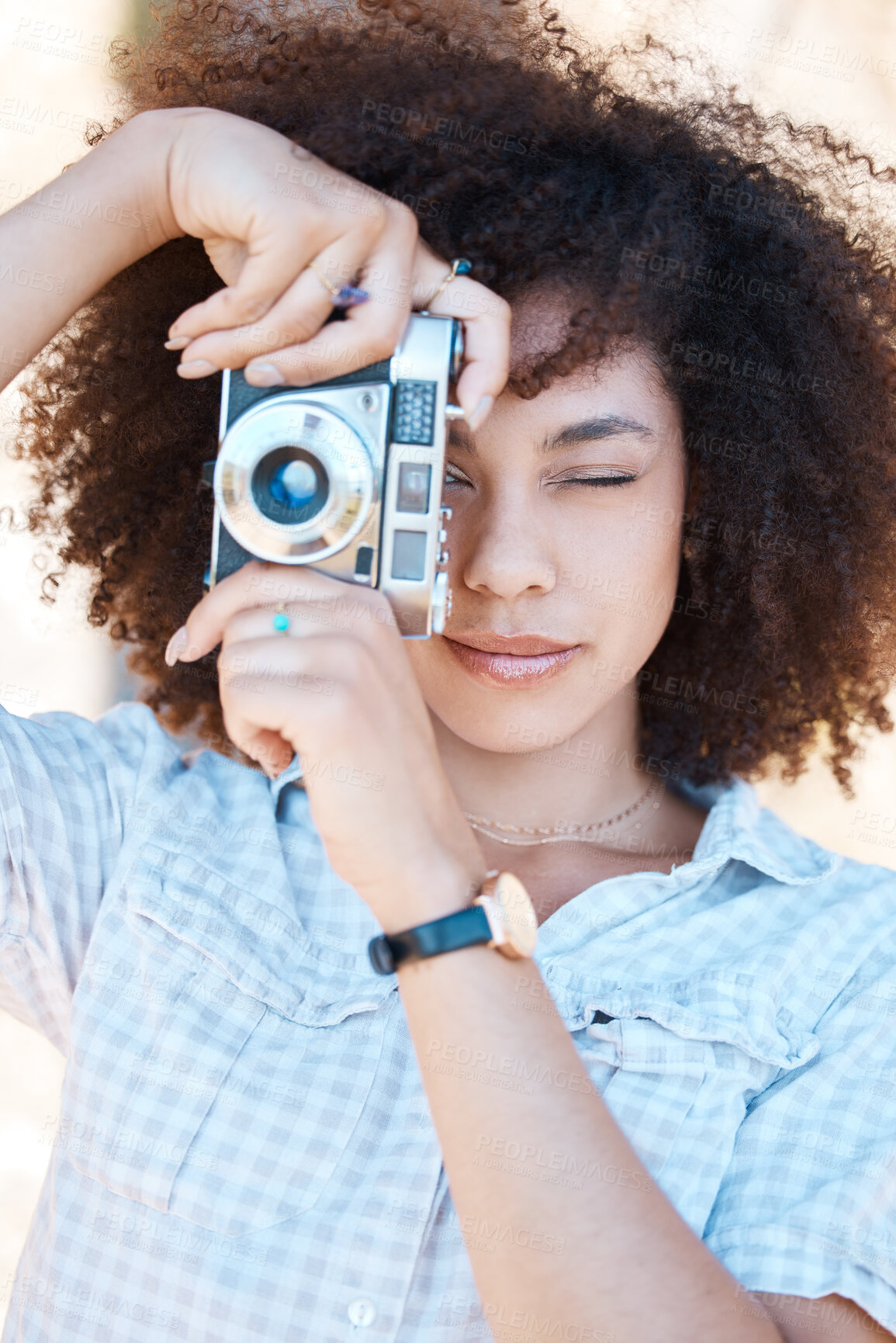 Buy stock photo Young mixed race woman with curly hair taking creative photos on a vintage retro film camera. One female photographer looking in viewfinder while capturing pictures as a hobby or profession on a shoot