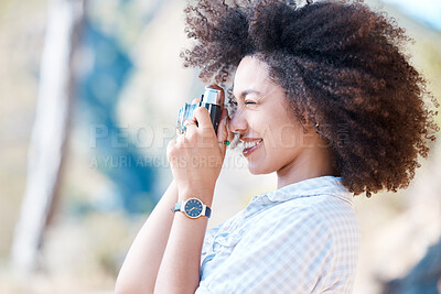 Buy stock photo One young smiling mixed race woman with afro holding and using a camera to take photographs. Happy hispanic woman with curly hair taking pictures outside. Passionate and skilled in hobby photography