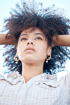 Buy stock photo Closeup shot of a beautiful young mixed race female with her hands in her afro. Below shot of one african american woman looking thoughtful and contemplative while standing outside. Full of ideas