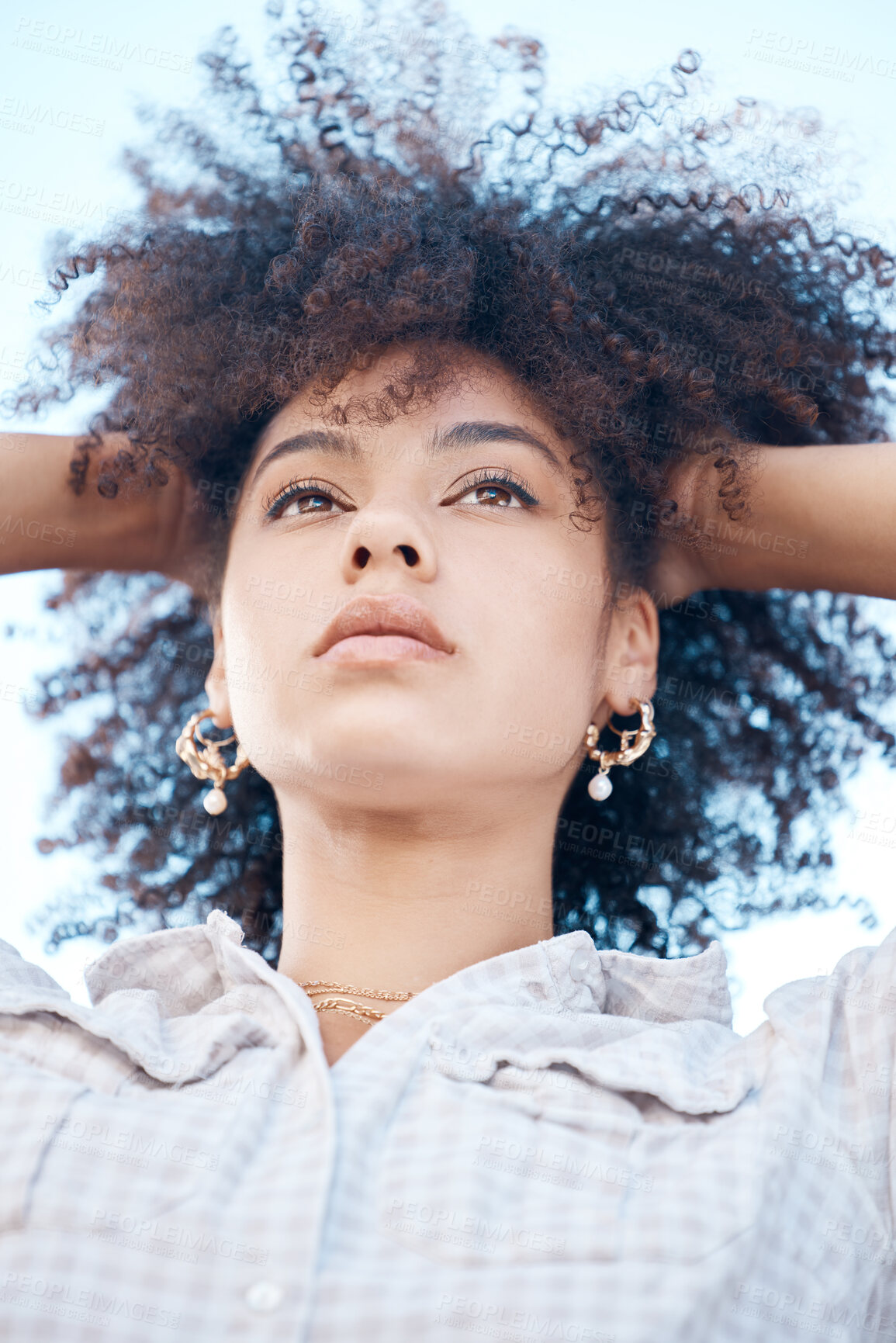 Buy stock photo Closeup shot of a beautiful young mixed race female with her hands in her afro. Below shot of one african american woman looking thoughtful and contemplative while standing outside. Full of ideas