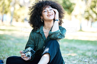 Young mixed race woman with a curly afro sitting in a park with her digital camera in hand. Young happy hispanic female photographer sitting in nature seeking inspiration and photo opportunities