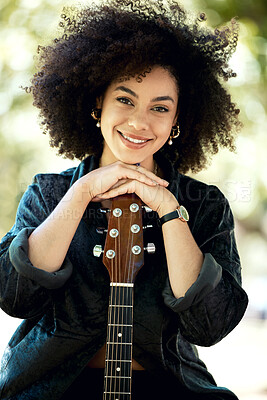 Young mixed race woman enjoying playing a guitar in the park in nature. Happy hispanic female with a curly afro holding a guitar while relaxing alone in a park