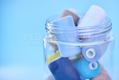 Multiple rolls of different and brightly coloured sewing thread in a seethrough glass jar isolated on a blue background in studio. A sewing kit for all your stitching and professional tailoring needs