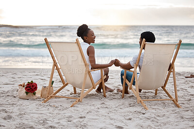 Buy stock photo Happy african American couple spending a day at the sea together. Content boyfriend and girlfriend holding hands while sitting on the beach. Caring husband and wife bonding on the seashore